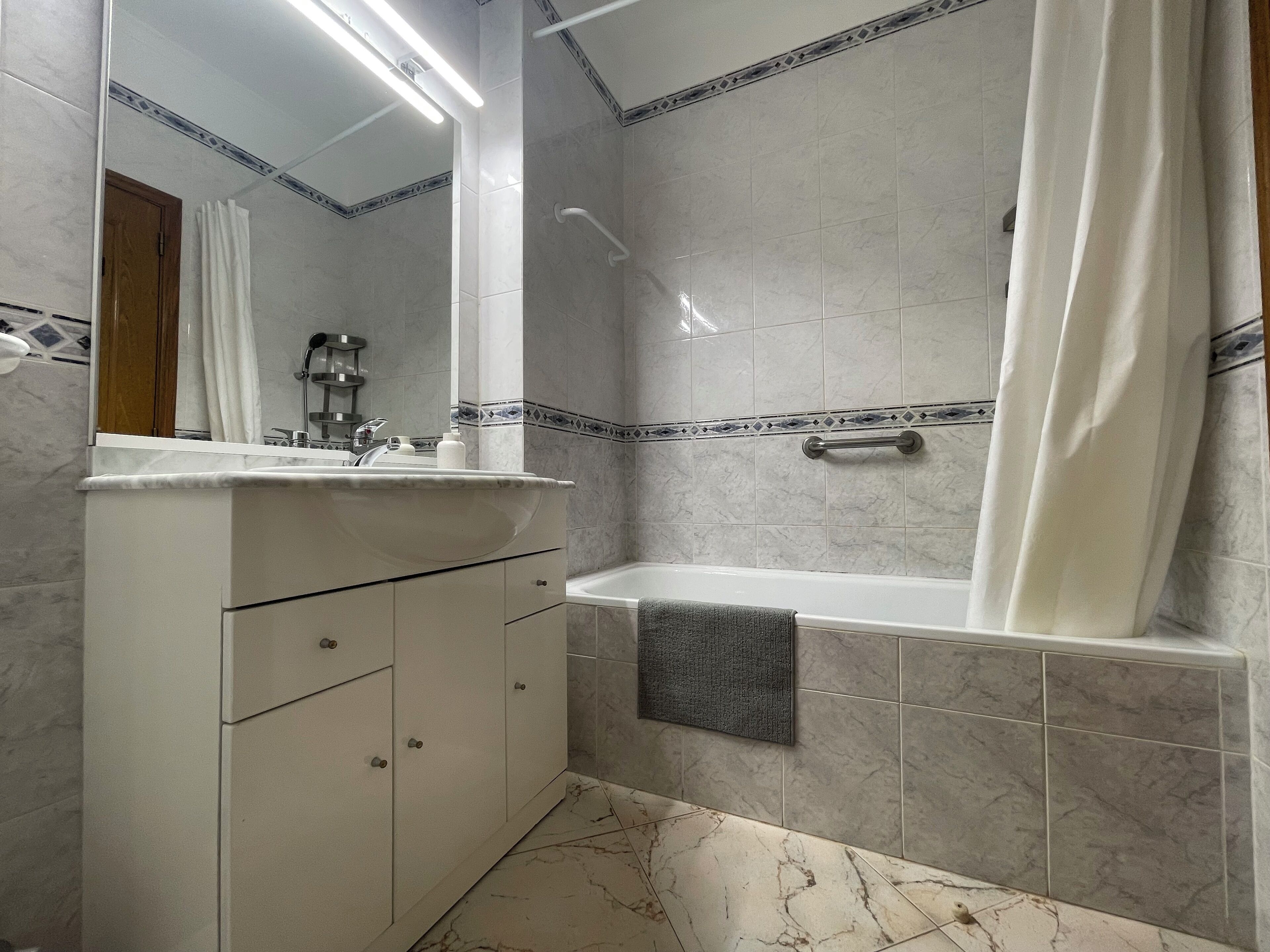 Un baño con una bañera, un lavabo con espejo y una toalla colgada en la pared.