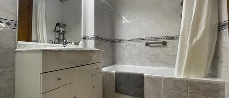 Un baño con una bañera, un lavabo con espejo y una toalla colgada en la pared.