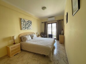 A hotel room with a bed, a nightstand, a chair, a desk, and a large window with curtains.