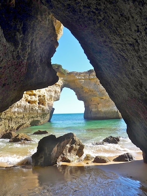A natural rock arch formation with clear blue water and sandy beach below.