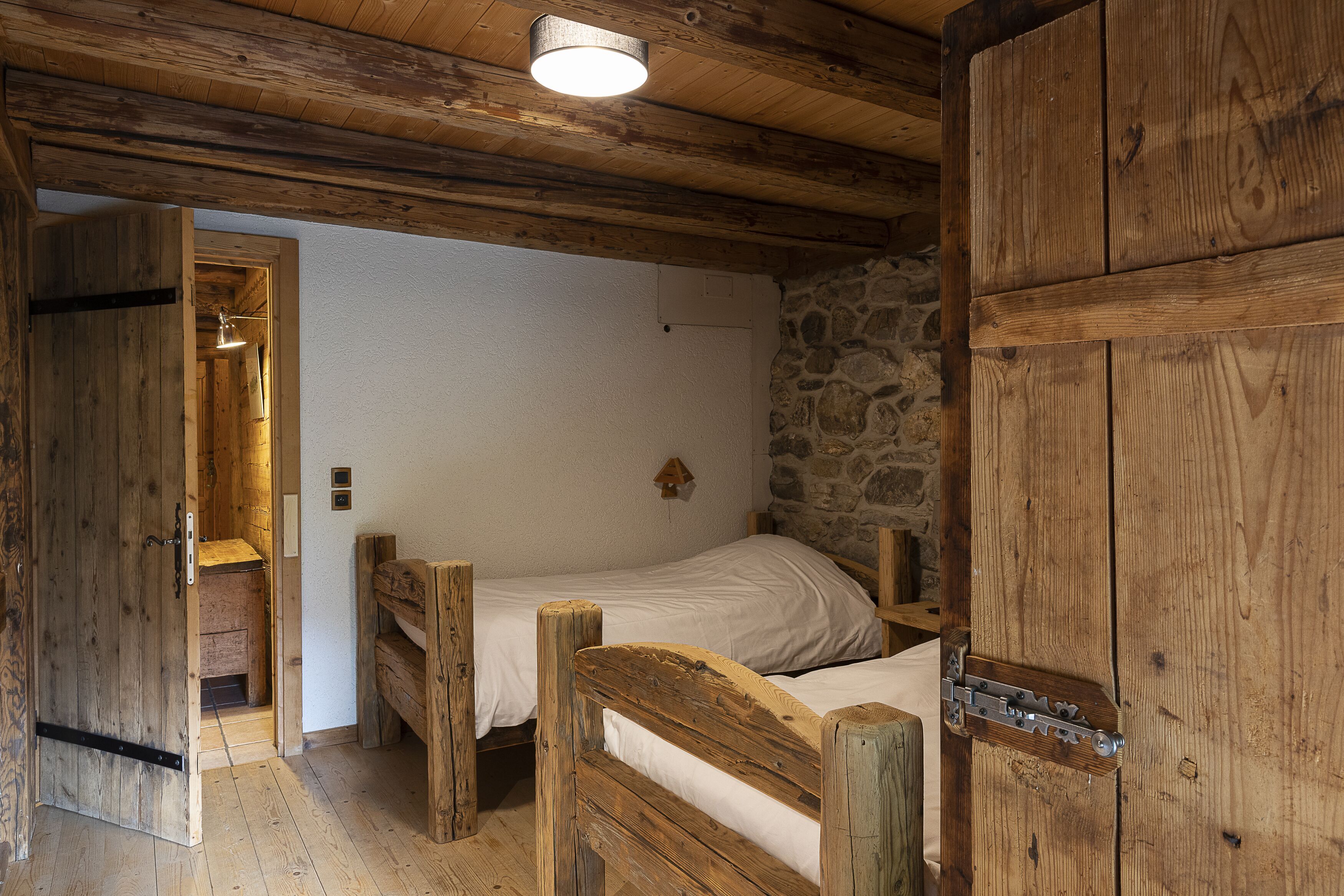 A rustic wooden room with a single bed, a stone wall, and a wooden door.