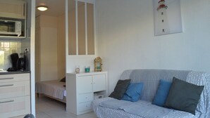 A compact room with a kitchenette, a bed, a white wardrobe, and a grey sofa with patterned cushions. - Studio Cabine 3 Couchages à 50m de la Plage avec Terrasse et Parking - Le Grau d'Agde (Le Grau d'Agde)