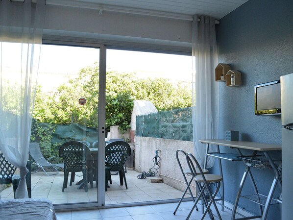 A balcony with a glass door, a table, chairs, and a TV mounted on the wall. - Studio Cabine 3 Couchages à 50m de la Plage avec Terrasse et Parking - Le Grau d'Agde (Le Grau d'Agde)