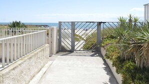 A concrete pathway leading to a beach with a metal gate. - Studio Cabine 3 Couchages à 50m de la Plage avec Terrasse et Parking - Le Grau d'Agde (Le Grau d'Agde)