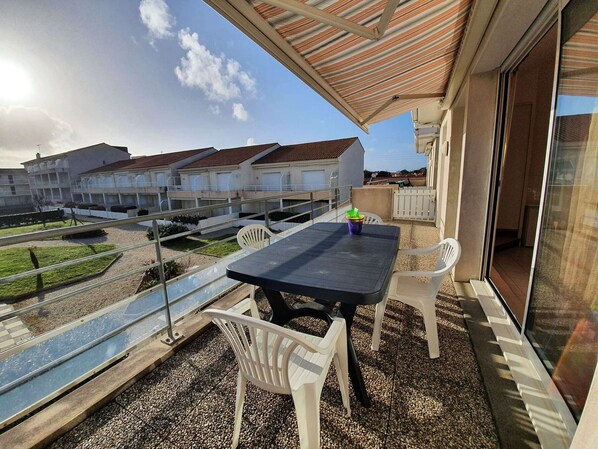 Varanda com mesa e cadeiras, com vista para uma área residencial com vários edifícios.