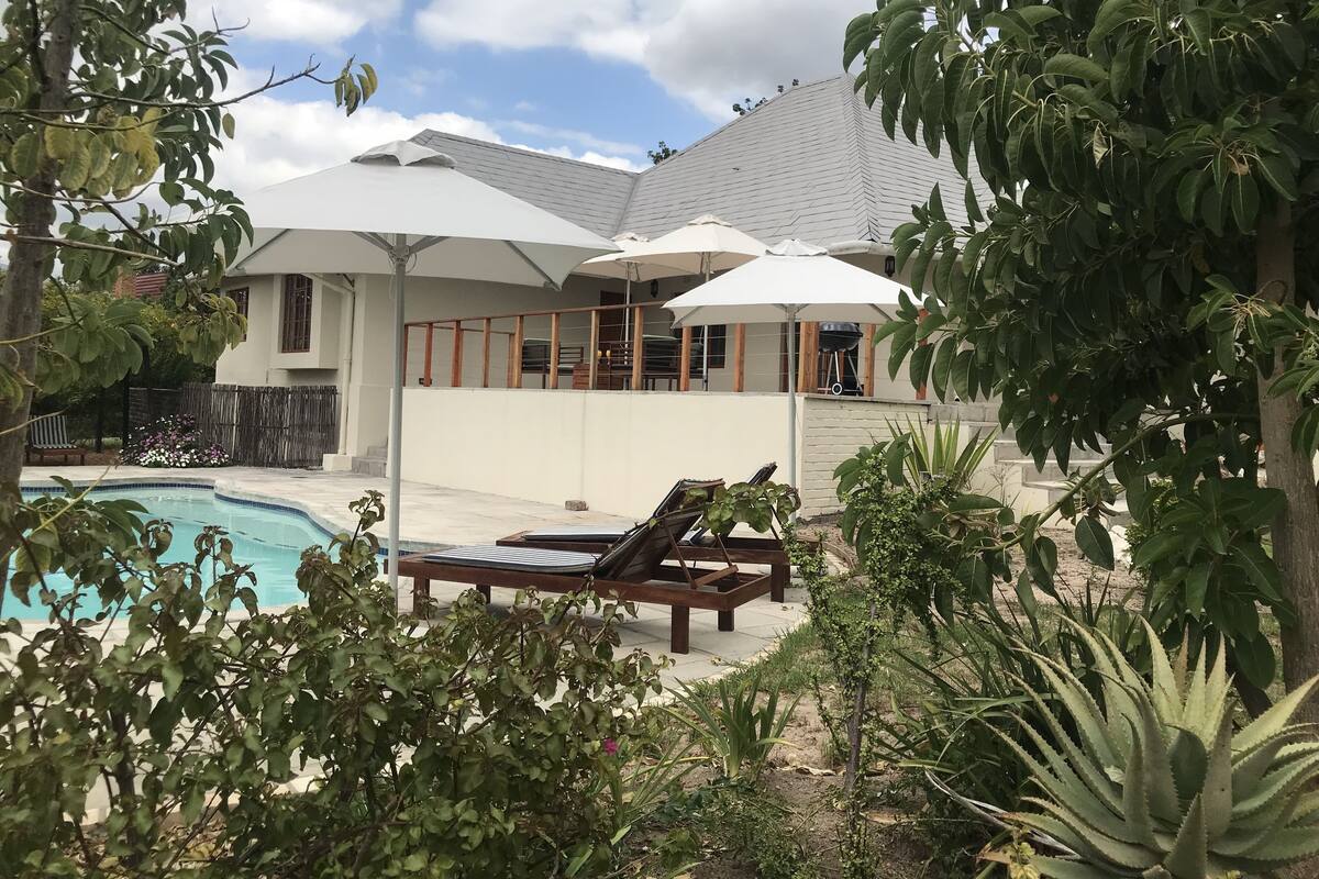 A poolside area with lounge chairs and umbrellas, a covered patio, and a view of the house.