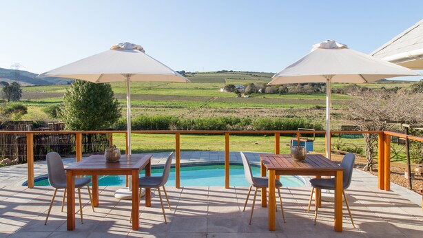 Een terras buiten met een zwembad, tafels en stoelen, met uitzicht op een schilderachtig landschap.