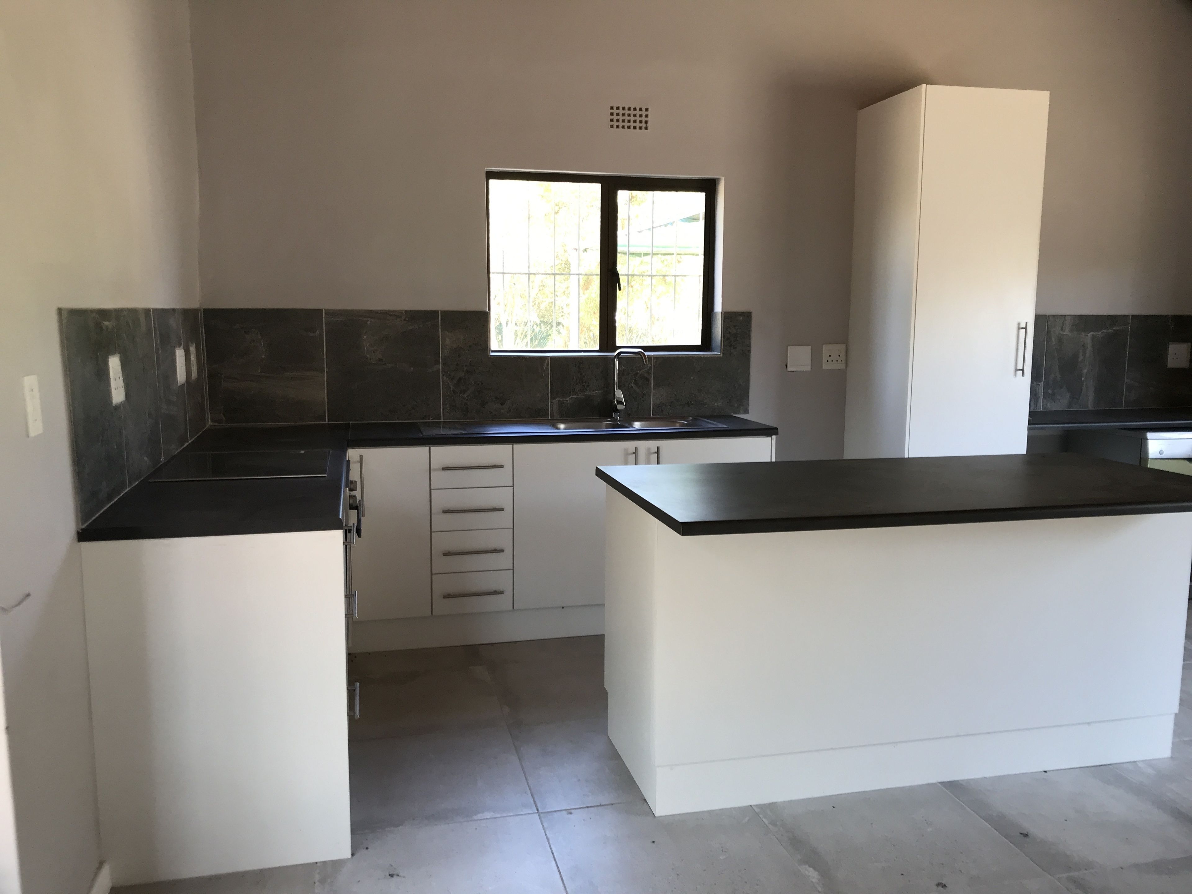 Una cocina moderna con una isla central, muebles blancos, encimera negra y una ventana sobre el fregadero.