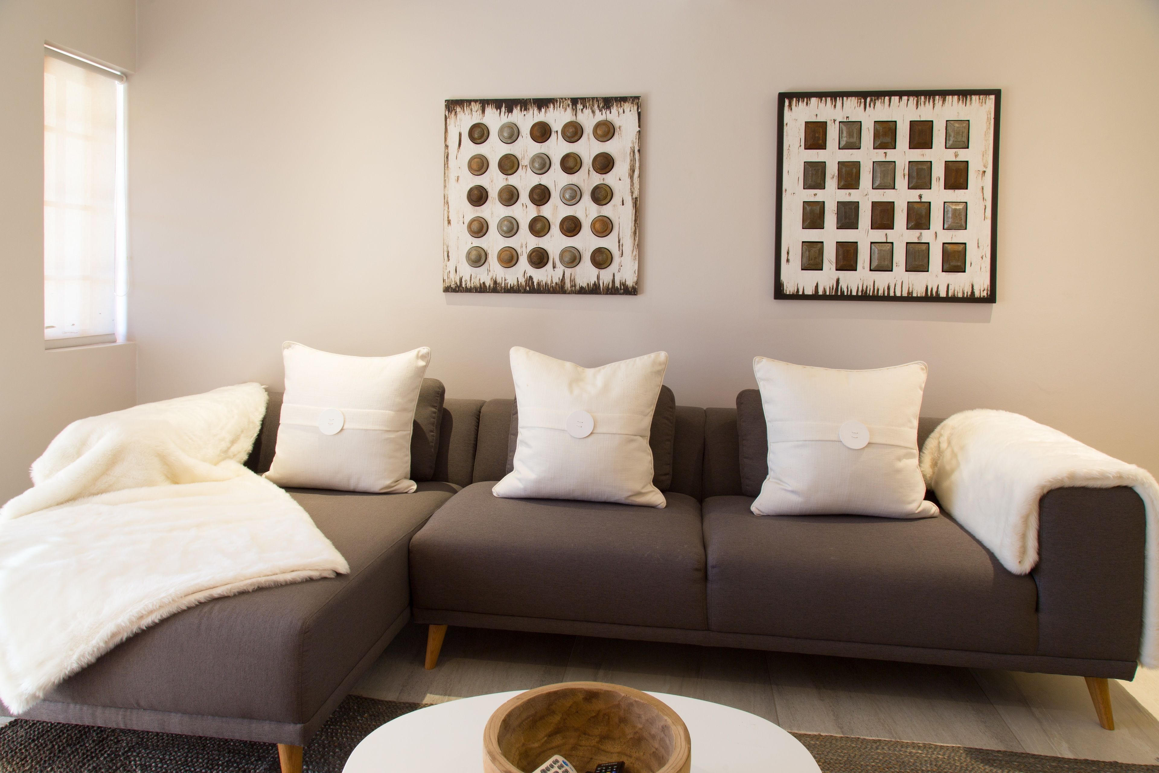 A modern living room with a brown sectional sofa, white cushions, and two wall art pieces.