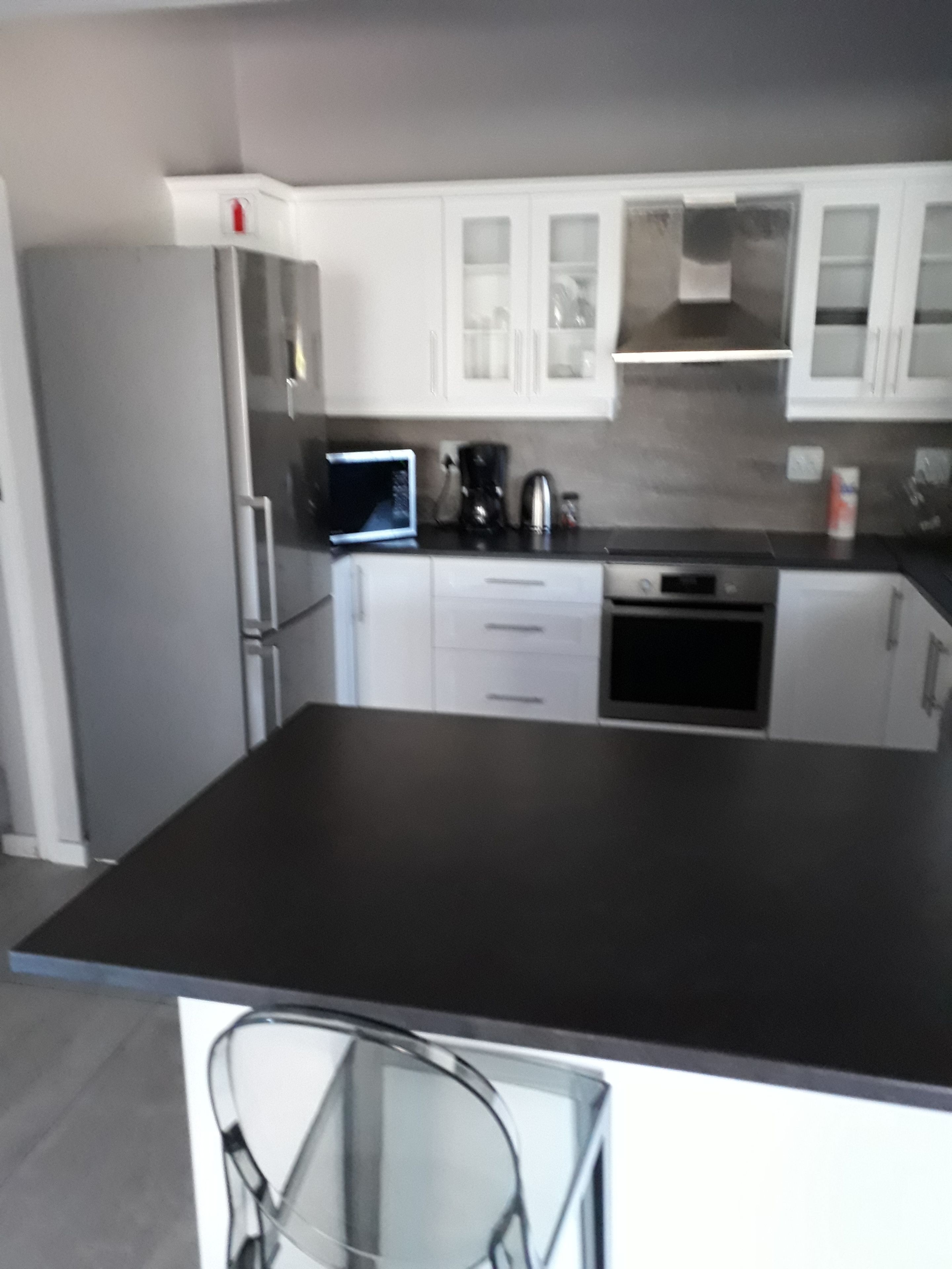 Una cocina moderna con armarios blancos, encimera negra y electrodomésticos de acero inoxidable.