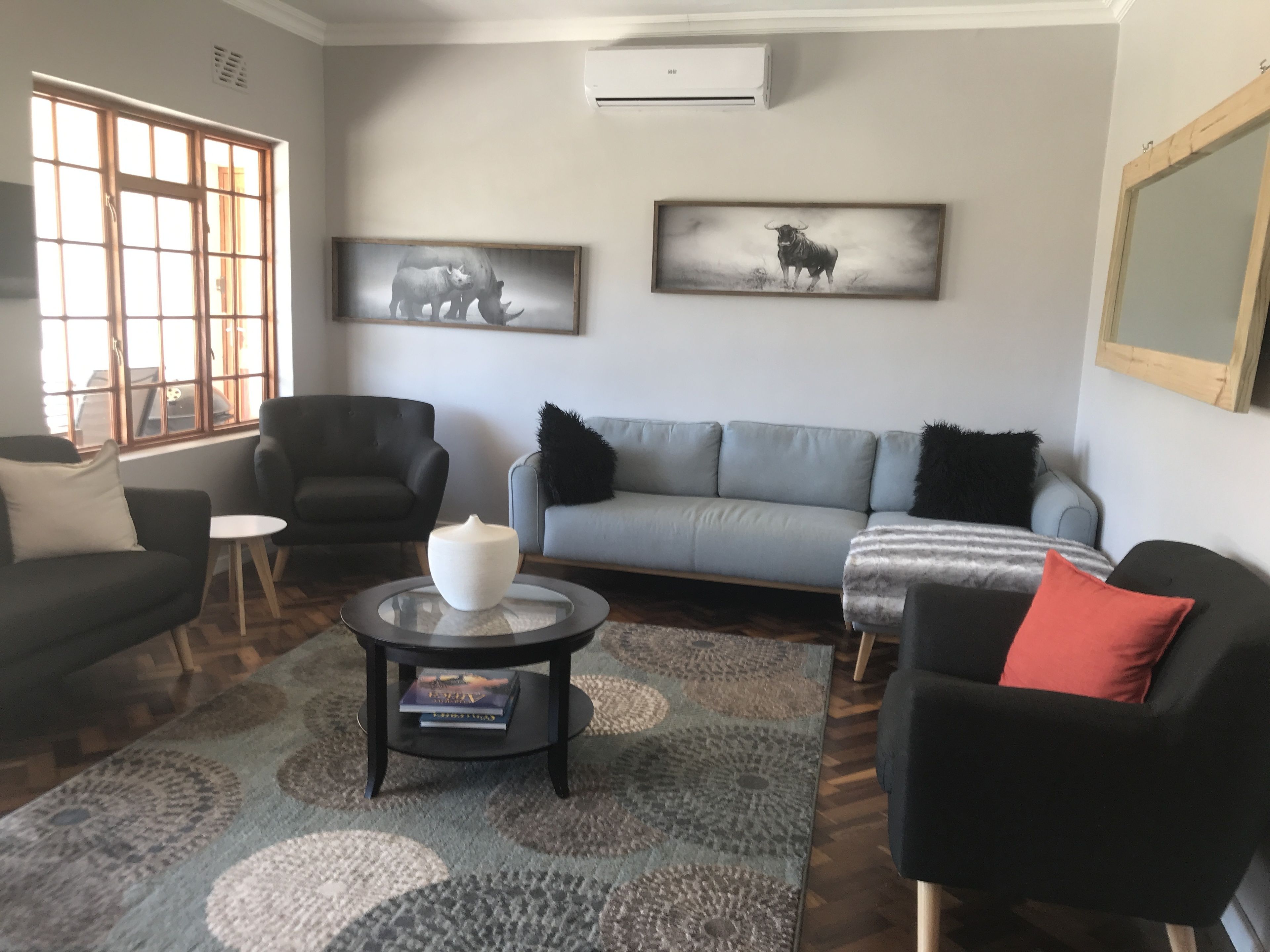 A living room with a grey sofa, black armchairs, a coffee table with books, and two wall-mounted animal paintings.