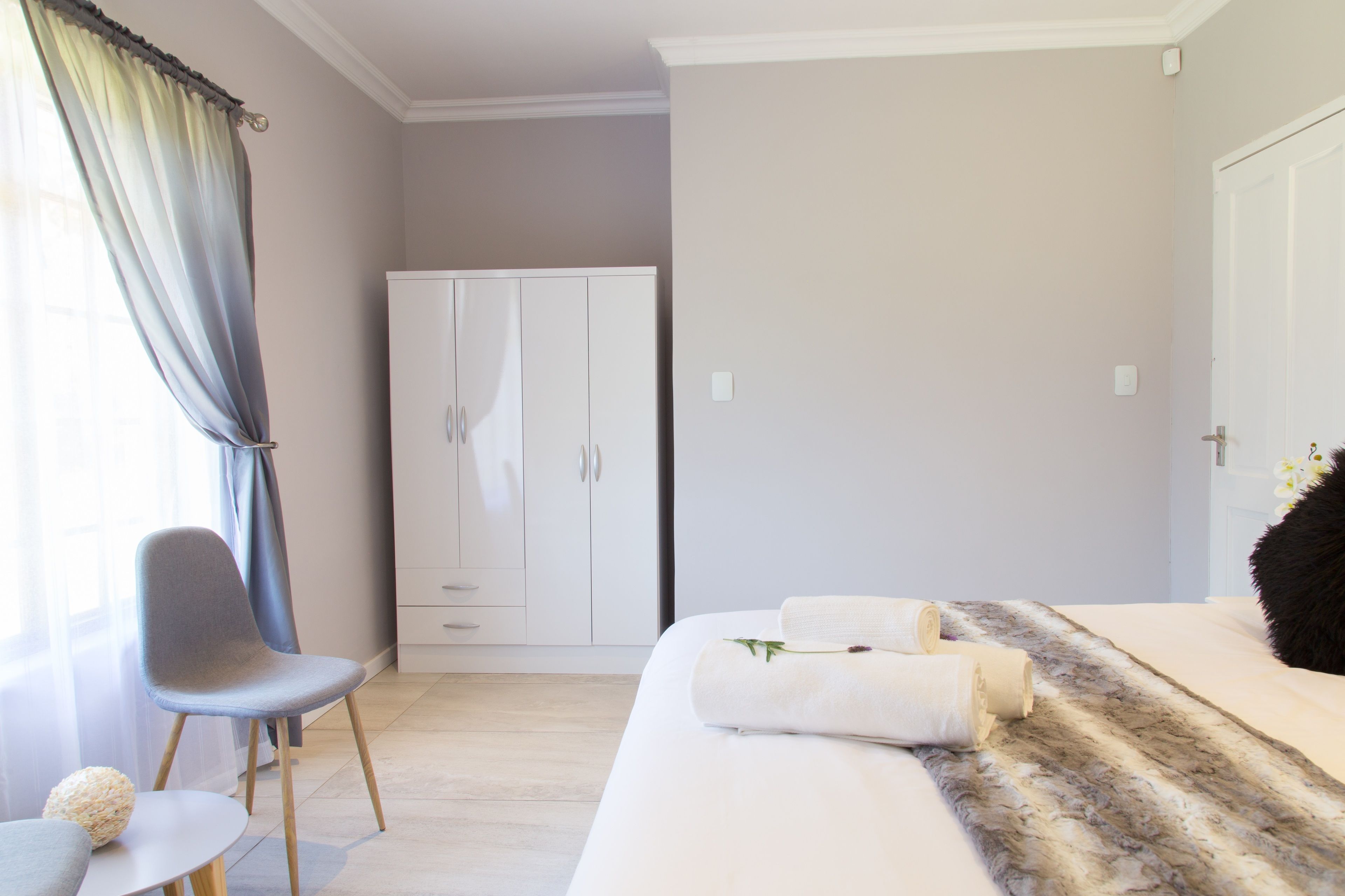 A bedroom with a bed, a chair, a wardrobe, and a small table.