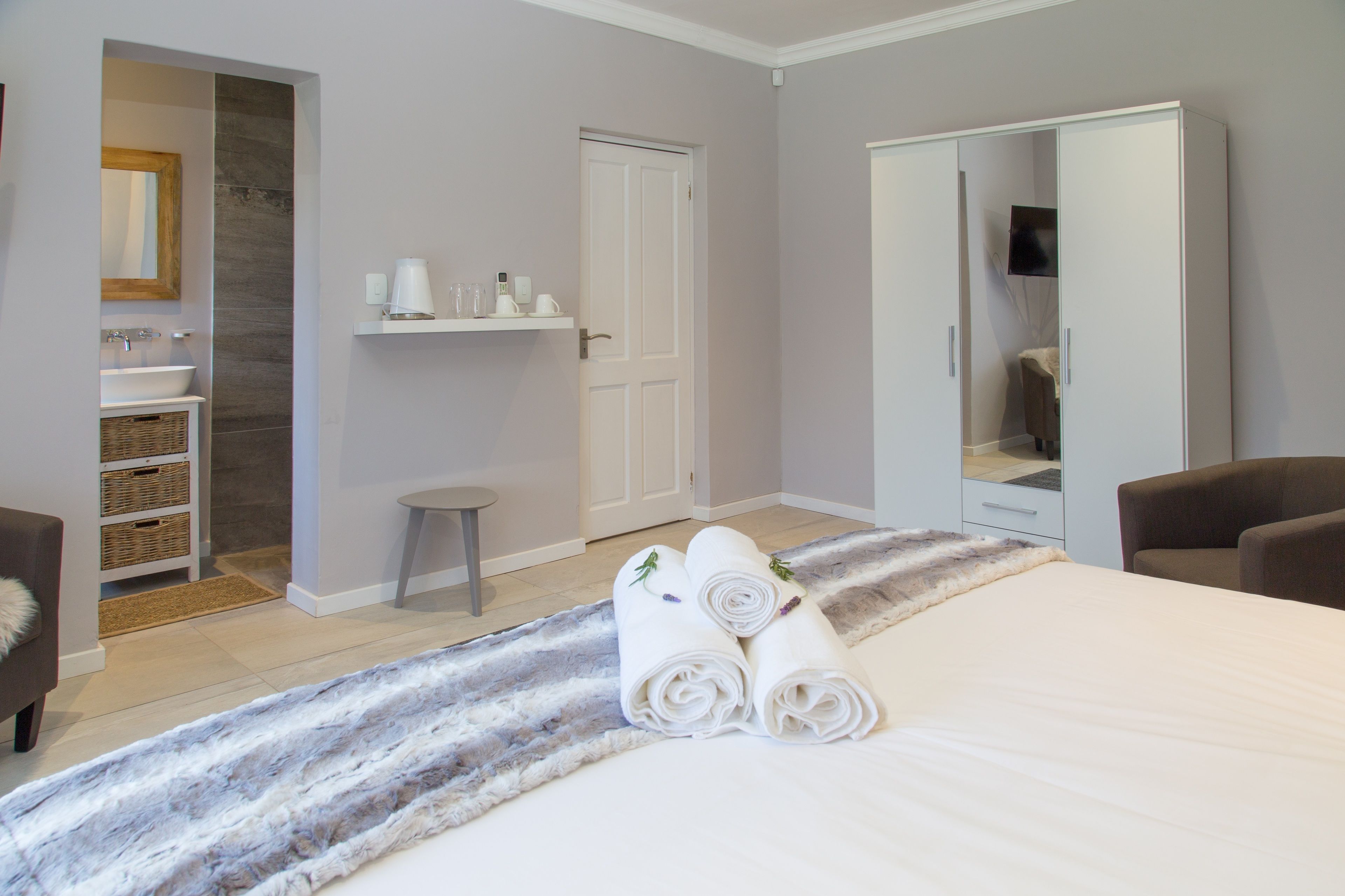 A hotel room with a bed, a bathroom with a sink and mirror, a wardrobe, and a small stool.