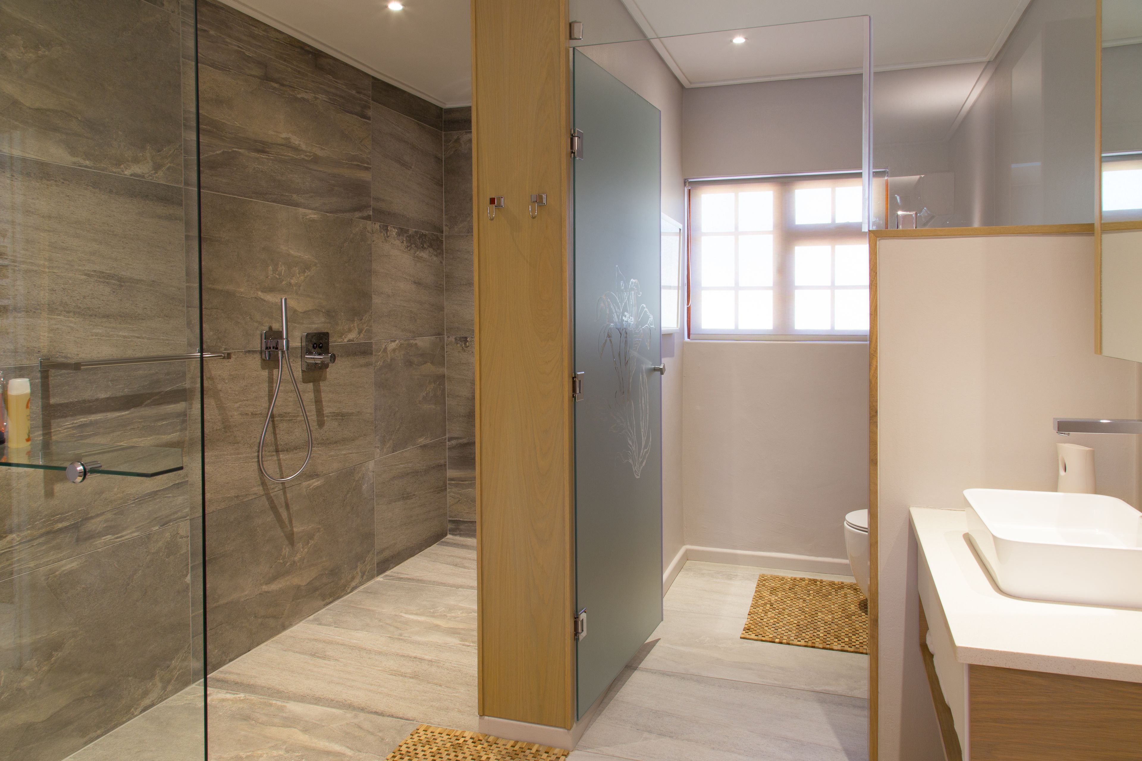 Une salle de bain moderne avec une douche à parois de verre, une porte en bois, un lavabo blanc et des toilettes.