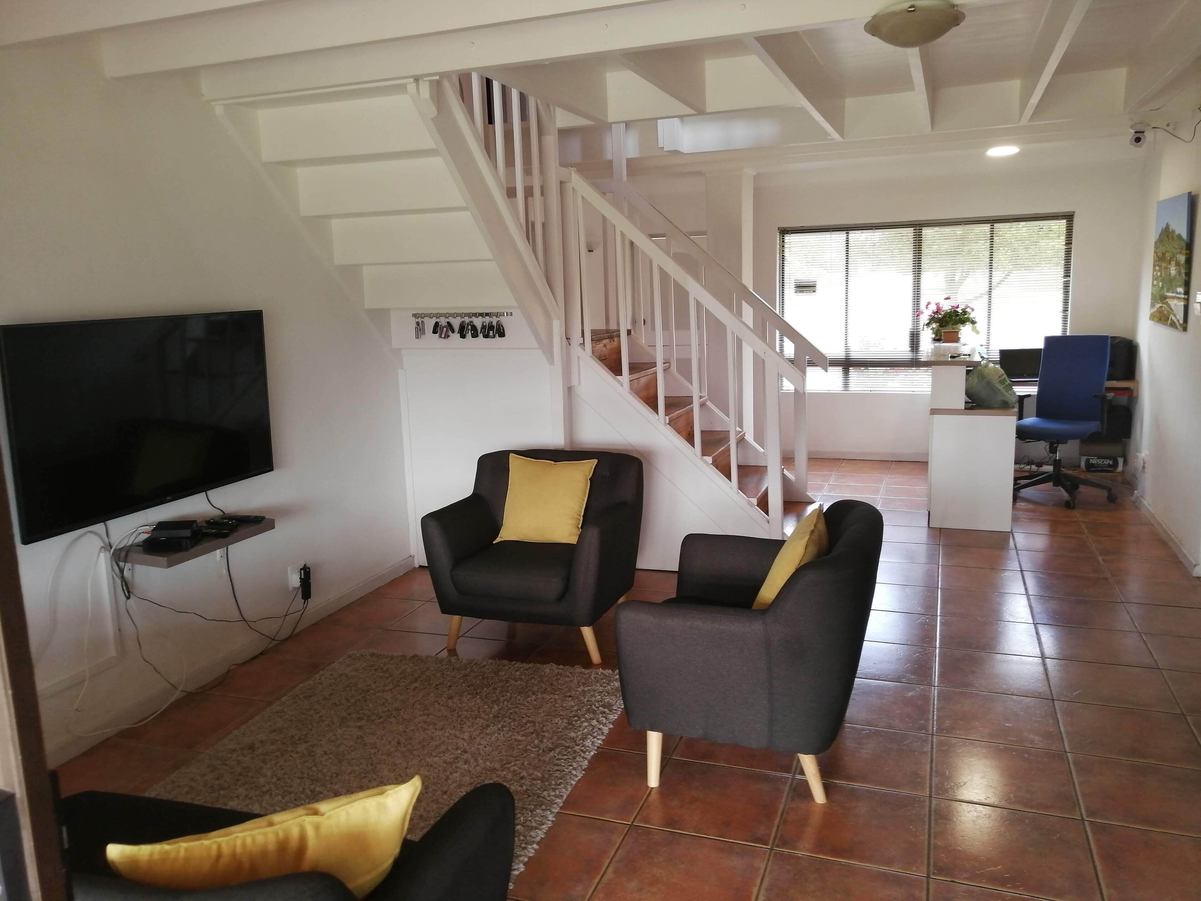 Een woonkamer met een televisie, twee fauteuils, een vloerkleed en een trap.