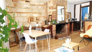 Un salon chaleureux avec une cheminée en briques, un coin repas avec une table et des chaises en bois, et une cuisine avec un comptoir et un miroir.