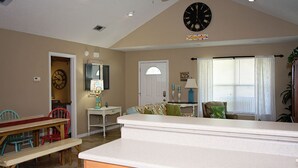 A living room with a dining area, a clock, and a door with a window. - Cottage house Near Beach/All Attractions 2/2 Super Clean Private (Gulf Shores)