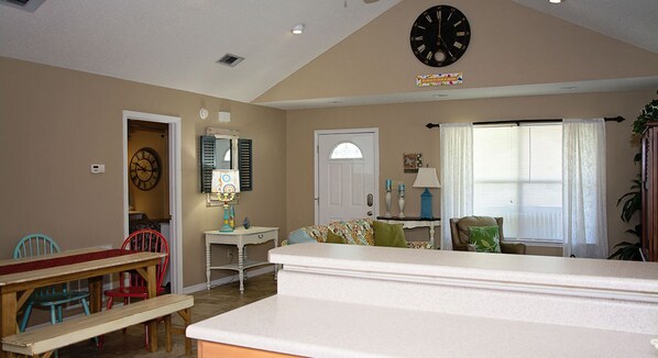 A living room with a dining area, a clock, and a door with a window.