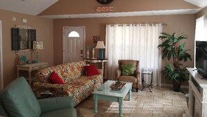 A living room with a floral sofa, a coffee table, a clock, a chair, a lamp, and a potted plant. - Cottage house Near Beach/All Attractions 2/2 Super Clean Private (Gulf Shores)
