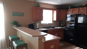 A kitchen with wooden cabinets, a black refrigerator, a coffee maker, and a sign that reads "Beach House". - Cottage house Near Beach/All Attractions 2/2 Super Clean Private (Gulf Shores)