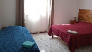 A bedroom with two beds, a wooden headboard, a nightstand, and a window with curtains.