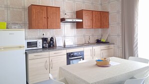 A modern kitchen with wooden cabinets, a built-in oven, a microwave, and a dining area with a table and chairs.
