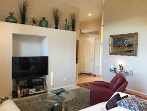 Una sala de estar con un televisor de pantalla plana, una mesa de centro de cristal, un sillón de cuero rojo, un sofá y un cuadro en la pared.