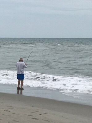 A person standing on a beach holding a fishing rod.