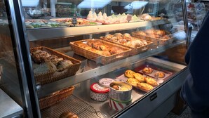 Una vitrina de panadería con diversos productos horneados, incluyendo pan, pasteles y tortas.