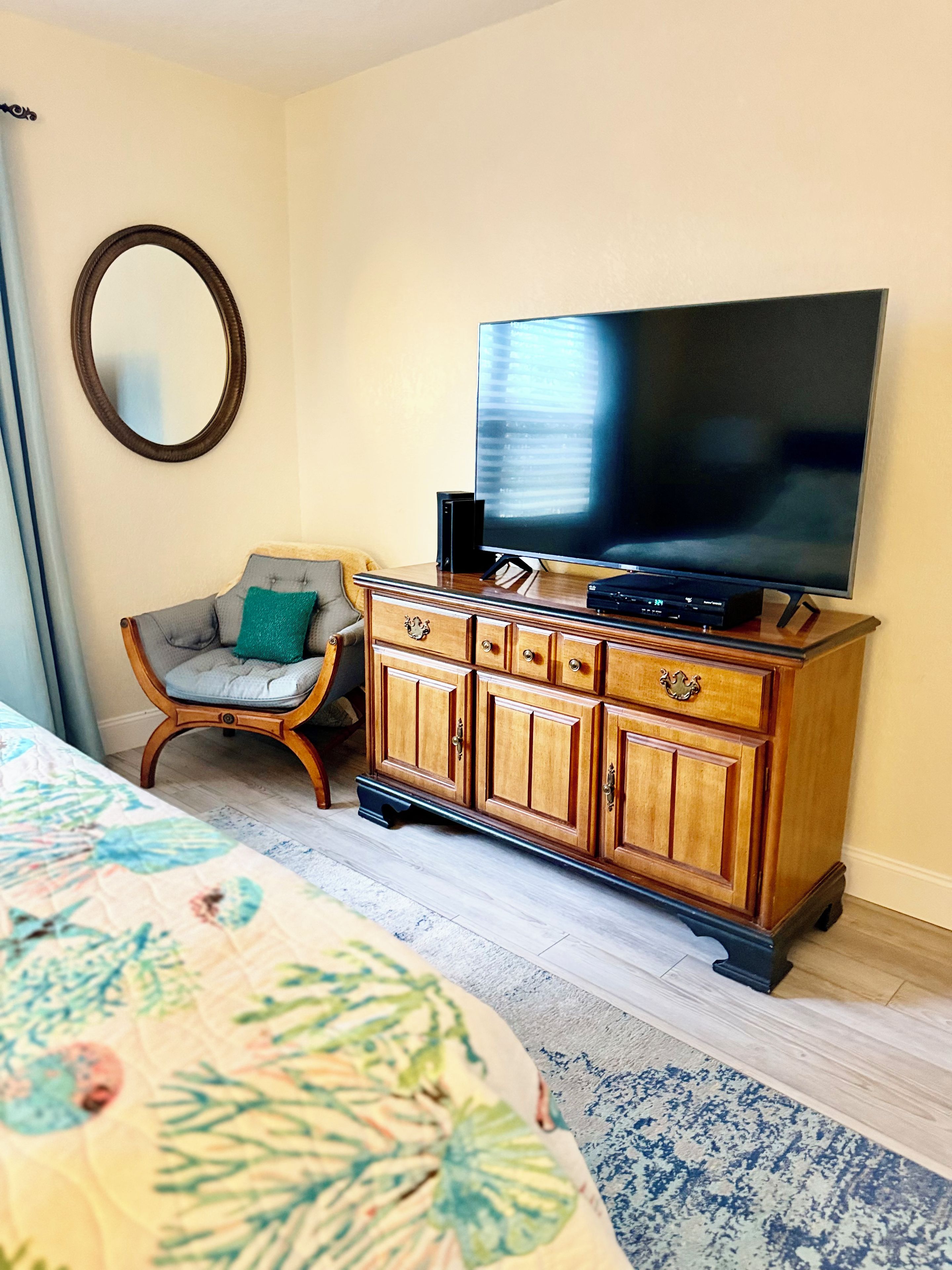 A bedroom with a bed, a wooden dresser, a television, and a chair.