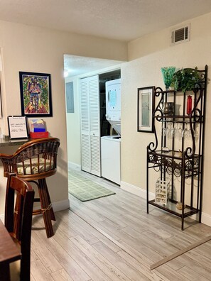 A room with a dining area, a metal rack with glasses, a framed painting, and a white appliance. - Oct stay 95 Nt: Full Kit, Patio, BBQ, Dine, Shop, Beach, Golf, Kayak (Melbourne)