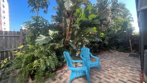Un patio con sillas de plástico azules, suelo de ladrillo y exuberante vegetación tropical.