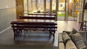 Un espace intérieur spacieux avec des bancs en bois et un canapé, de grandes fenêtres laissant entrer la lumière naturelle et une vue sur l’extérieur.