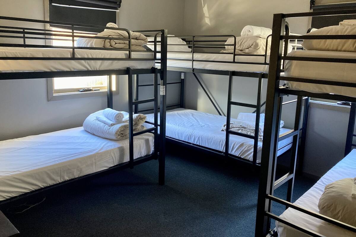 A dormitory room with bunk beds, a window, and a wall-mounted air conditioning unit.