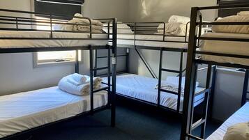 A dormitory room with bunk beds, a window, and a wall-mounted air conditioning unit.