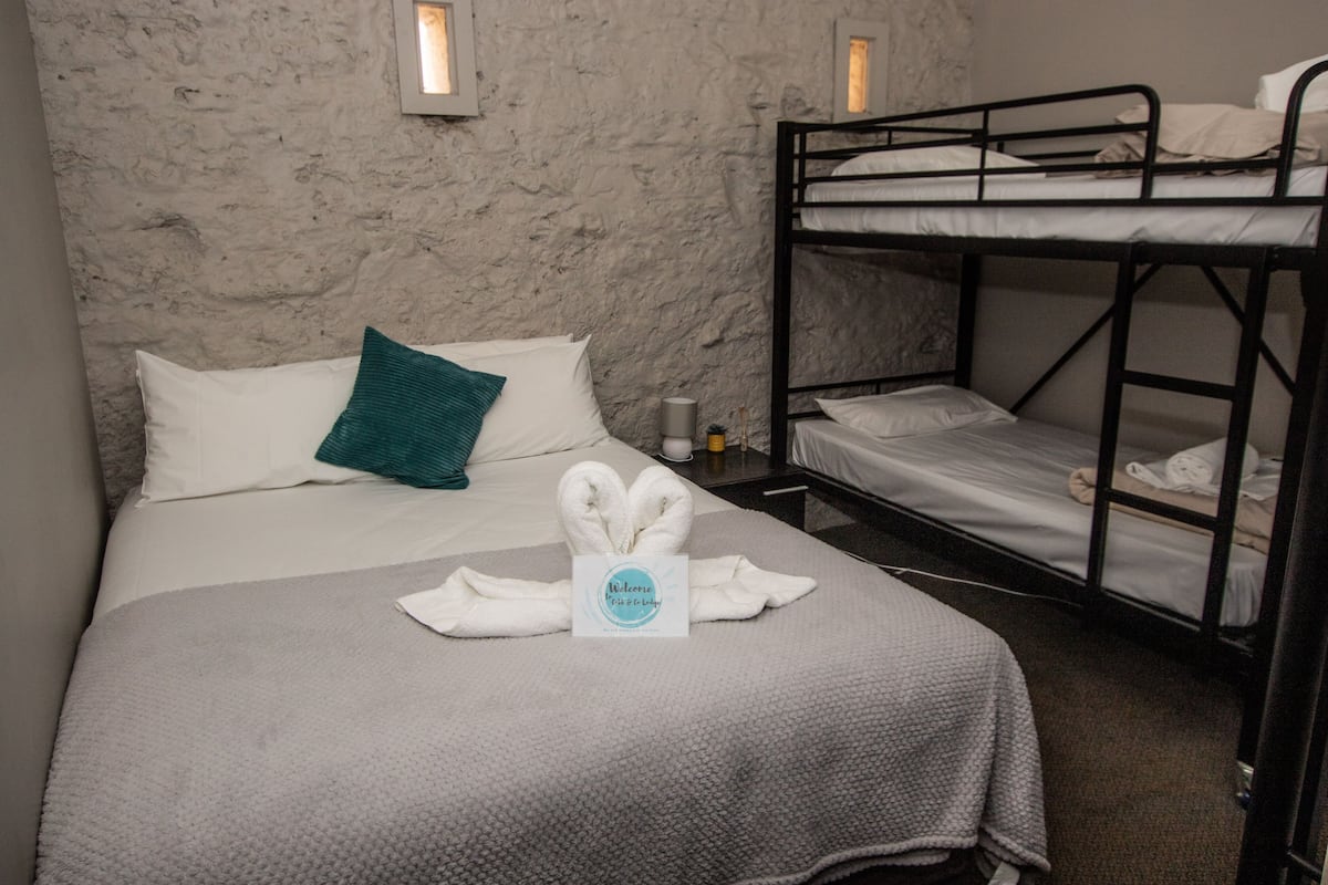 A room with a bunk bed, a single bed with a towel arrangement, and a textured wall.