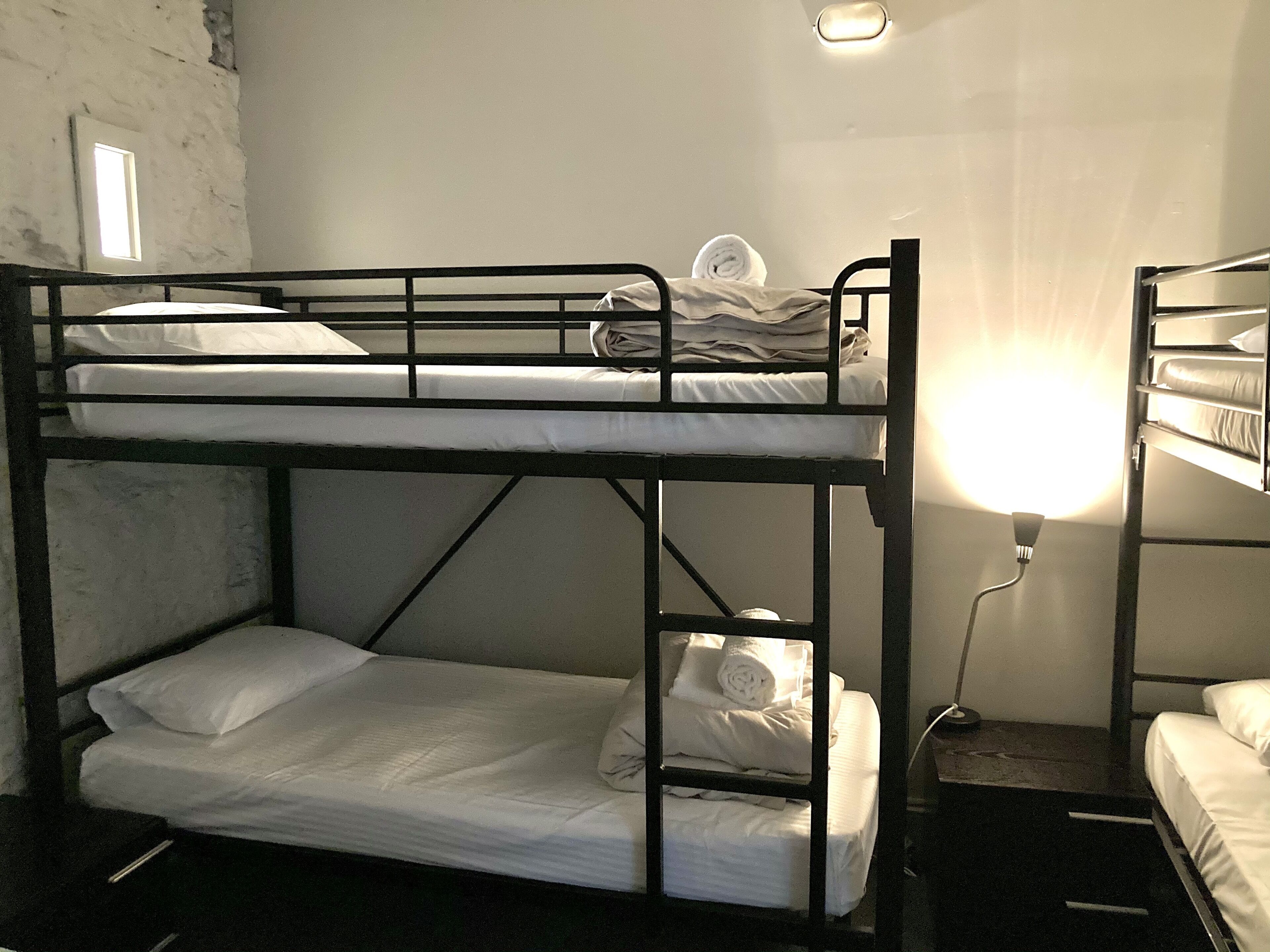Habitación con literas, una cama individual en la parte inferior y otra en la superior. Una lámpara está fijada a la pared en el lado derecho de la habitación.