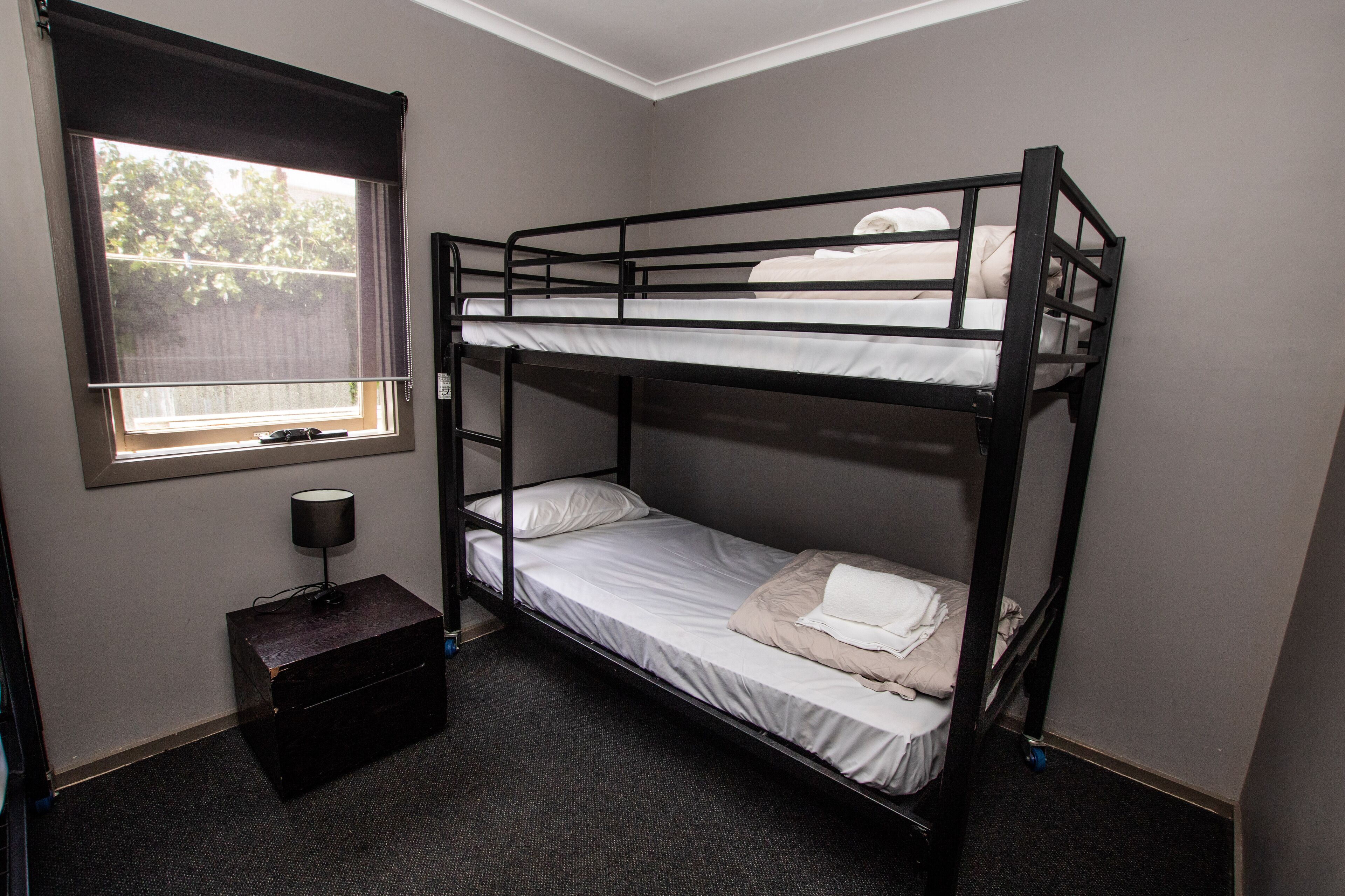 A bunk bed room with a window, a desk with a lamp, and a small storage box.