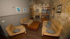 Un salon chaleureux avec des canapés en cuir, une table basse en bois et des étagères adossées à un mur en pierre.