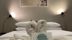 Un lit avec du linge de lit blanc, deux lampes de chevet, une serviette pliée posée sur le lit et un panneau d’accueil.