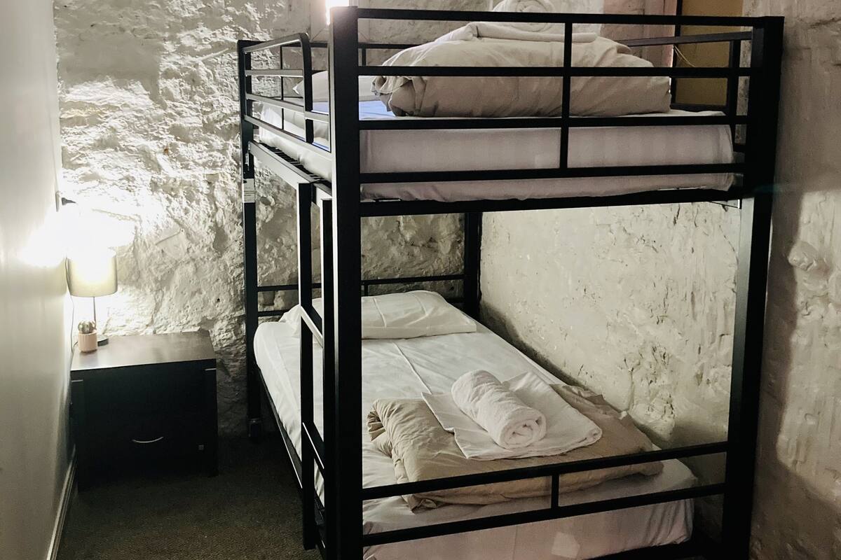 A bunk bed with a nightstand and a lamp in a room with textured white walls.