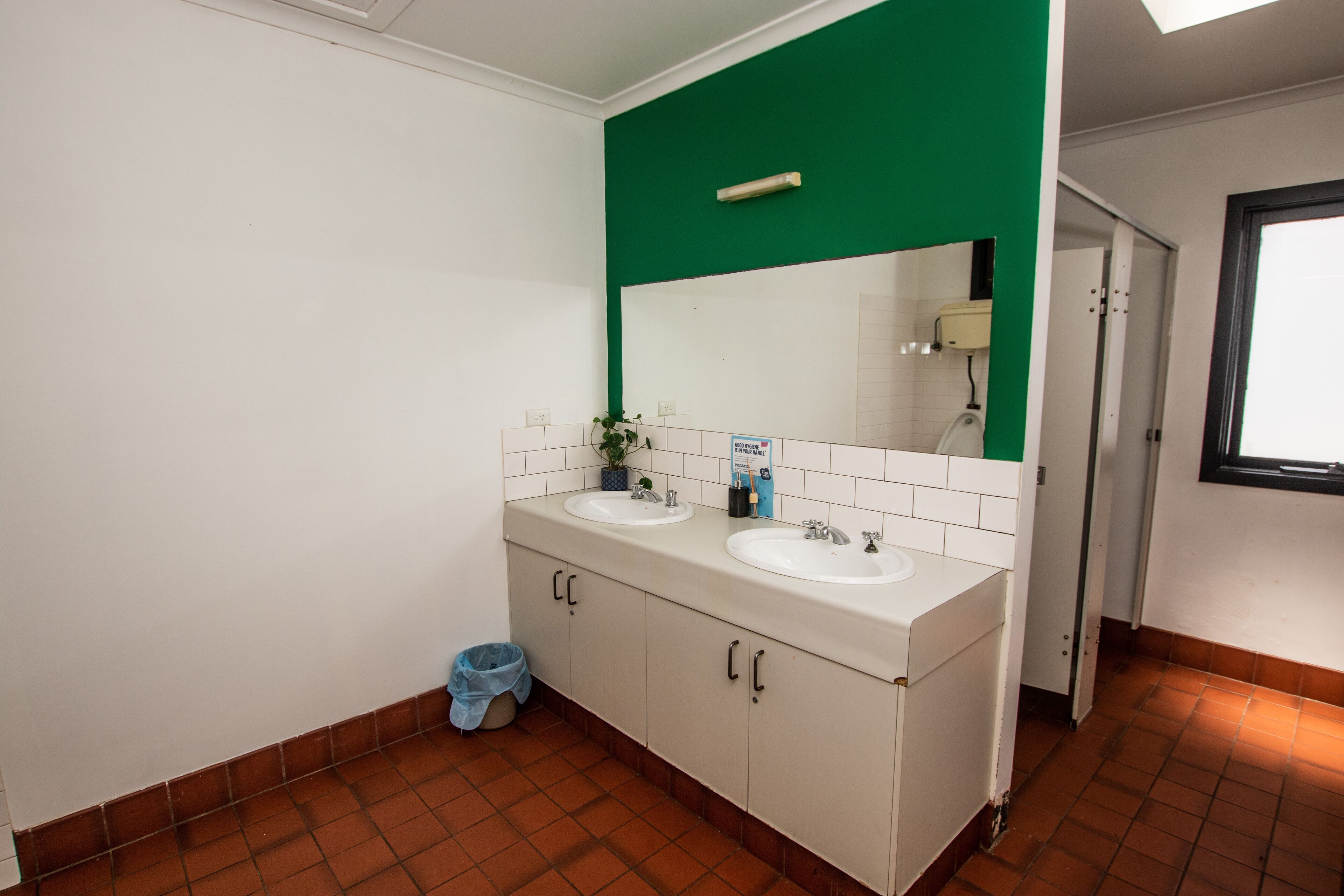 A bathroom with two sinks, a mirror, and a trash bin.