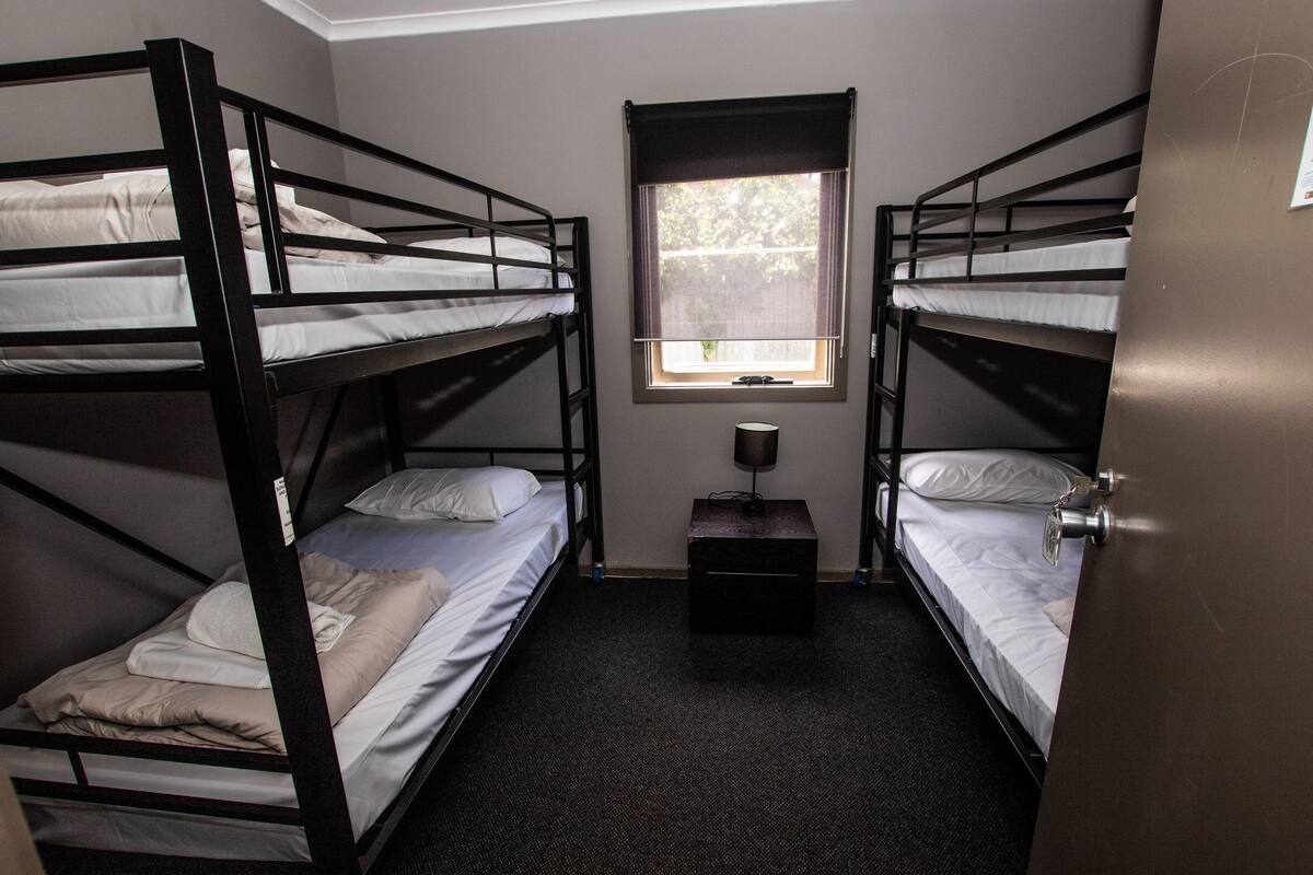 A room with two bunk beds, a small table, and a window.