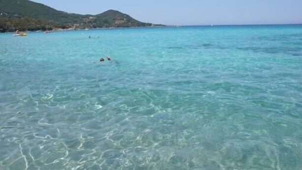 A clear turquoise sea with a hilly landscape in the background.