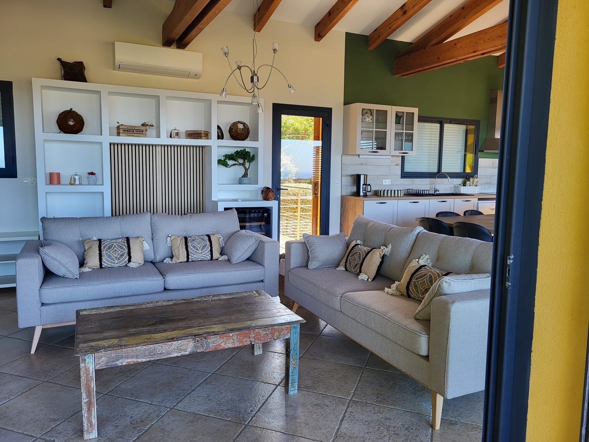 A modern living room with two sofas, a coffee table, and a built-in kitchen area visible through an open door.