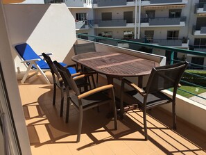 Un balcon avec une table ronde et des chaises, un fauteuil bleu et une vue sur un immeuble à plusieurs étages.