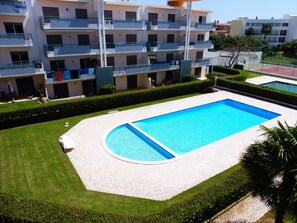 Une piscine entourée d’une zone dallée, avec un immeuble à plusieurs étages en arrière-plan.