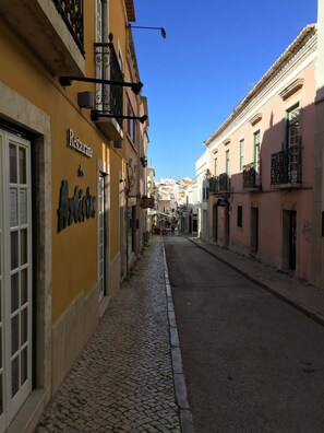 Une ruelle étroite pavée, bordée d’immeubles dotés de balcons et d’enseignes indiquant la présence d’un restaurant et d’un bar.