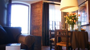 A cozy room with a sofa, a table with a vase of flowers, and a large window with curtains. - Saint Paul De Vence, Charming Suites in The Heart Of The Village. 4 ** Biloba (Saint-Paul-De-Vence)