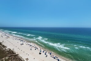 Ein Strand mit Reihen von Sonnenschirmen und Liegen, einem klaren Himmel und dem Meer.
